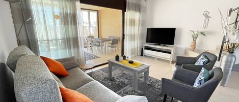 A modern living room with a sofa, armchair, coffee table, TV, and a dining area with chairs and a table.