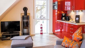 Una cocina moderna con armarios rojos, una chimenea y un televisor en un espacio de sala de estar con un sofá gris y almohadas naranjas.