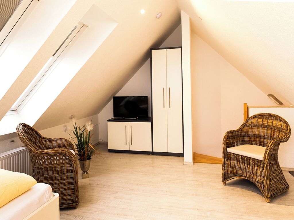 Une chambre de style loft moderne, avec un plafond en pente, une grande armoire, un téléviseur et deux fauteuils en osier.
