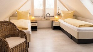 Un dormitorio cálido en el ático con dos camas, una silla de mimbre y un ventanal.
