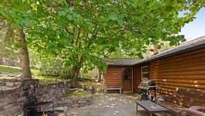 Una cabaña de madera con pared de piedra, asientos exteriores y zona de barbacoa.