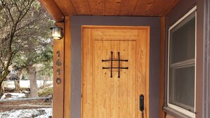 Una puerta de madera con una placa de número, un picaporte metálico y una ventana a la derecha.