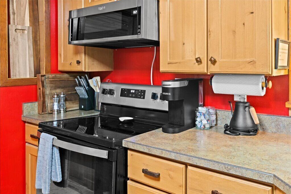 A kitchen with a black stove, a microwave, wooden cabinets, and a coffee maker.