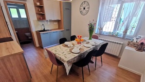 A dining area with a table set for four, a clock on the wall, and a window with curtains.