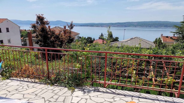 A terrace with a stone floor, a red metal railing, and a view of a lake and distant hills.