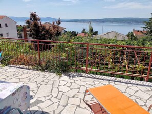 Una terrazza con pavimento in pietra, ringhiera in metallo rosso e vista su un lago e colline lontane.