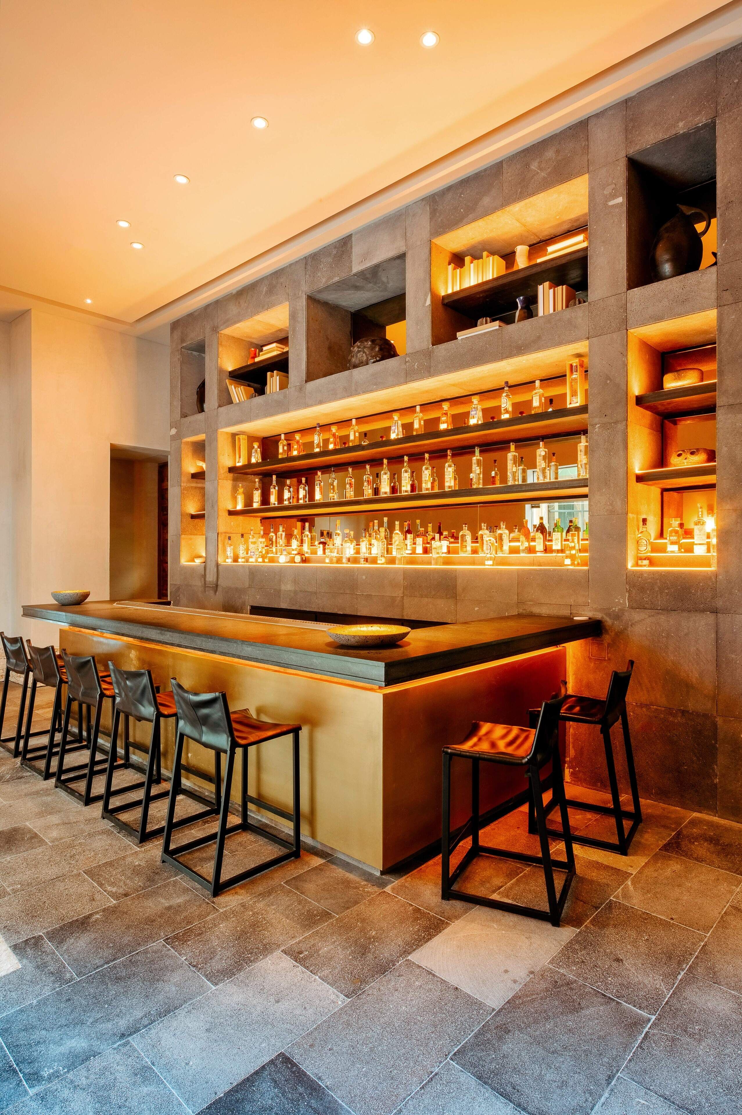 A bar area with multiple shelves of bottles, bar stools, and a counter.