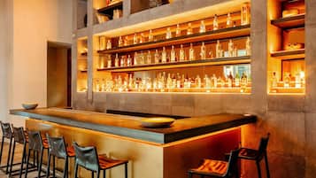 Zona de bar con estantes llenos de botellas, taburetes y mostrador.