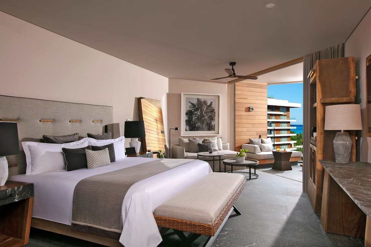 Una habitación de hotel moderna con una cama grande, un sofá, una mesita y un balcón con vistas al océano.