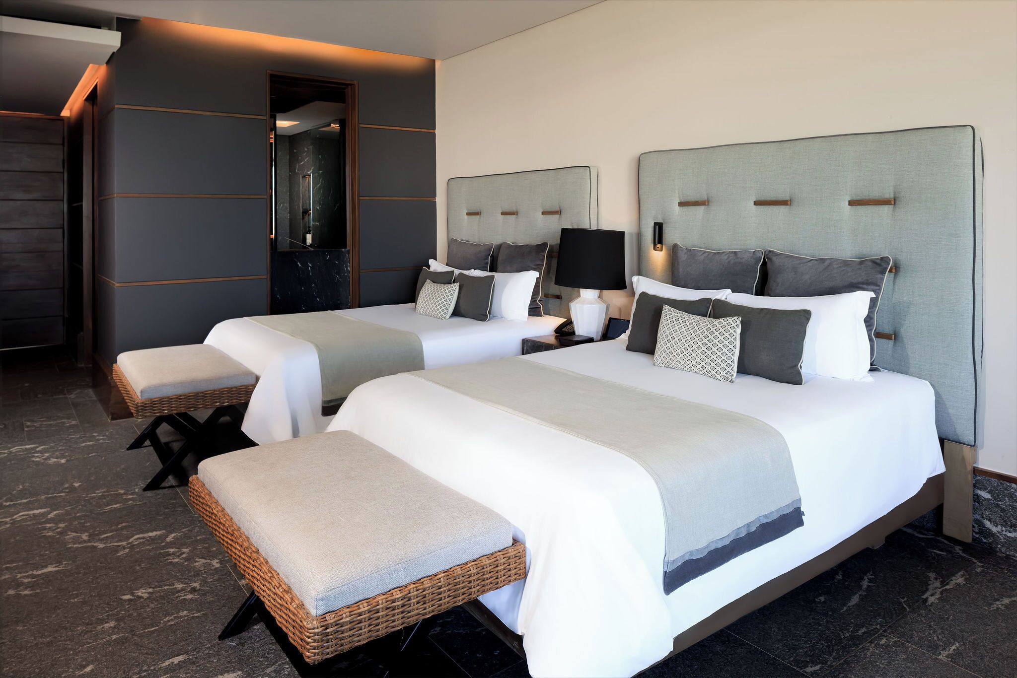 Een hotelkamer met twee bedden, elk voorzien van een hoofdbord, nachtkastjes en lampen. De kamer heeft een modern design met een marmeren vloer en een grote spiegel aan de muur.