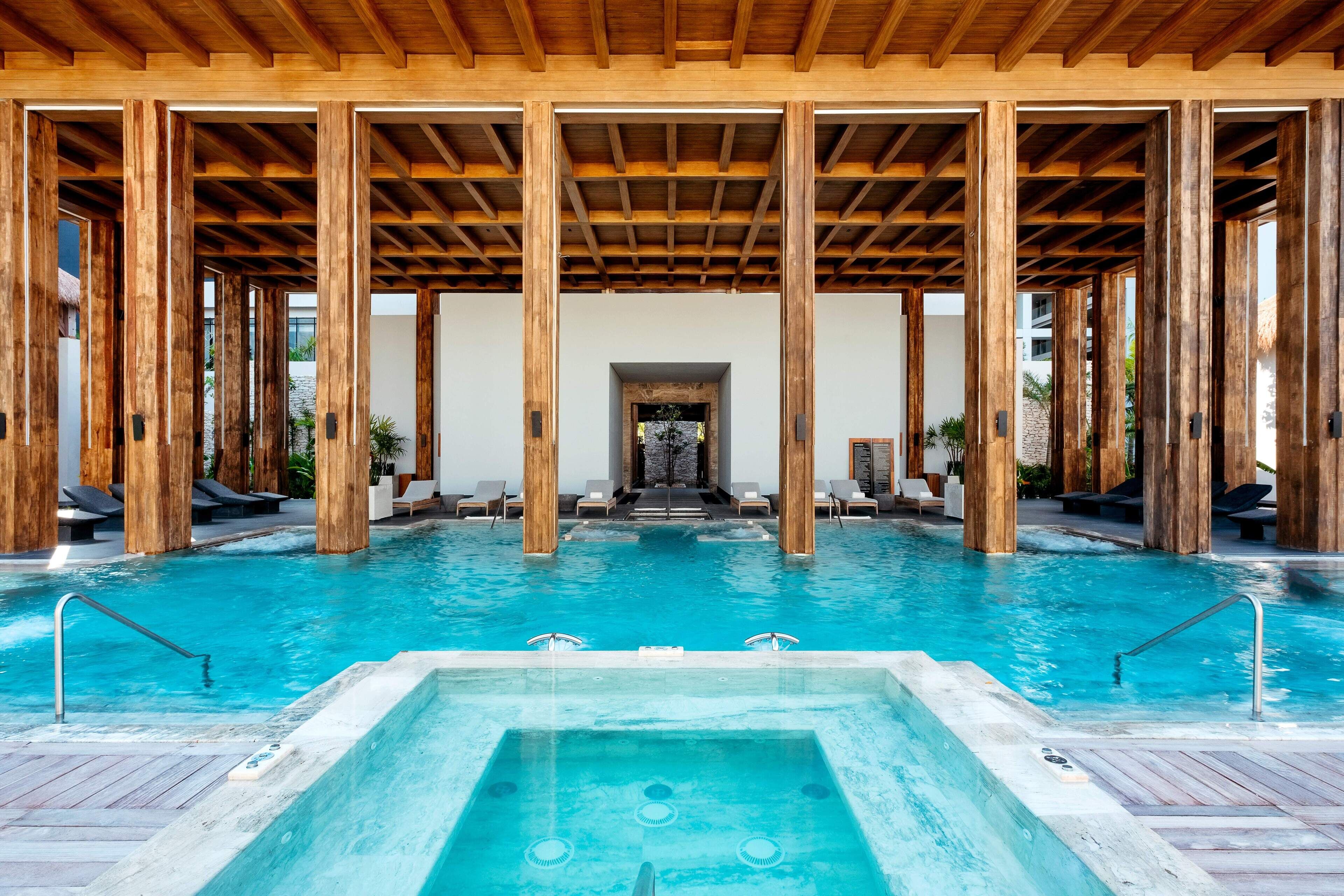 A pool area with wooden beams, lounge chairs, and a hot tub.