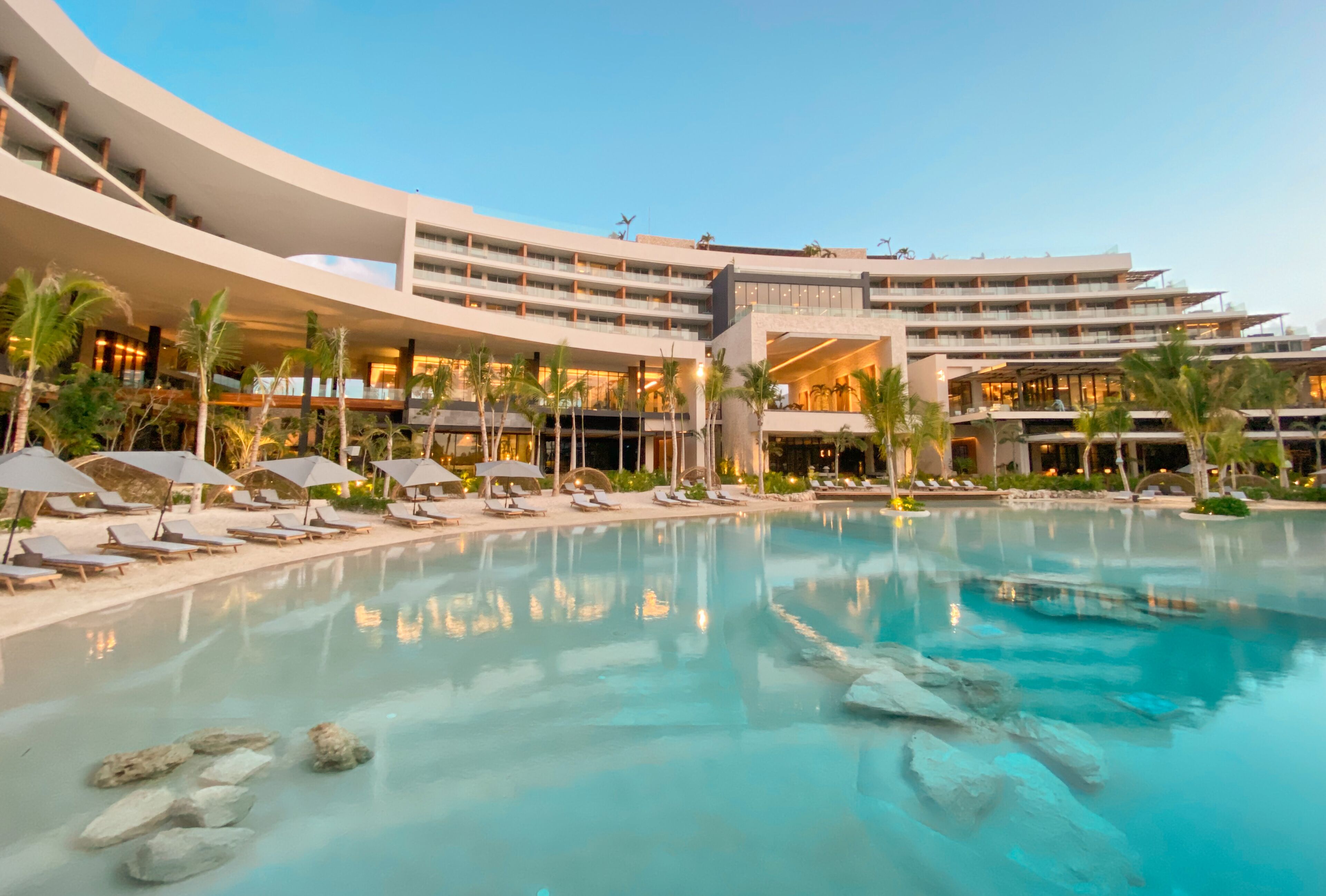 A modern hotel with a large pool, multiple balconies, and sun loungers.