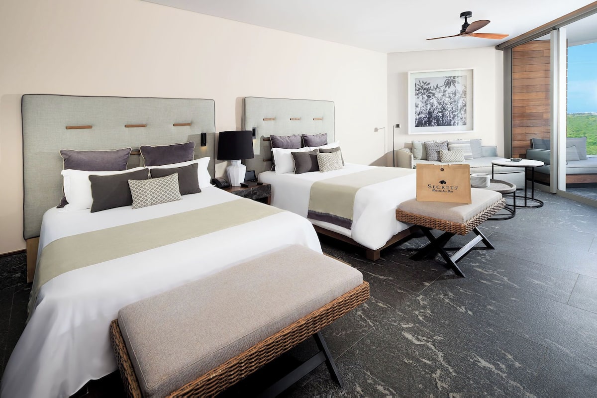 Habitación de hotel con dos camas, un balcón y vistas al exterior.