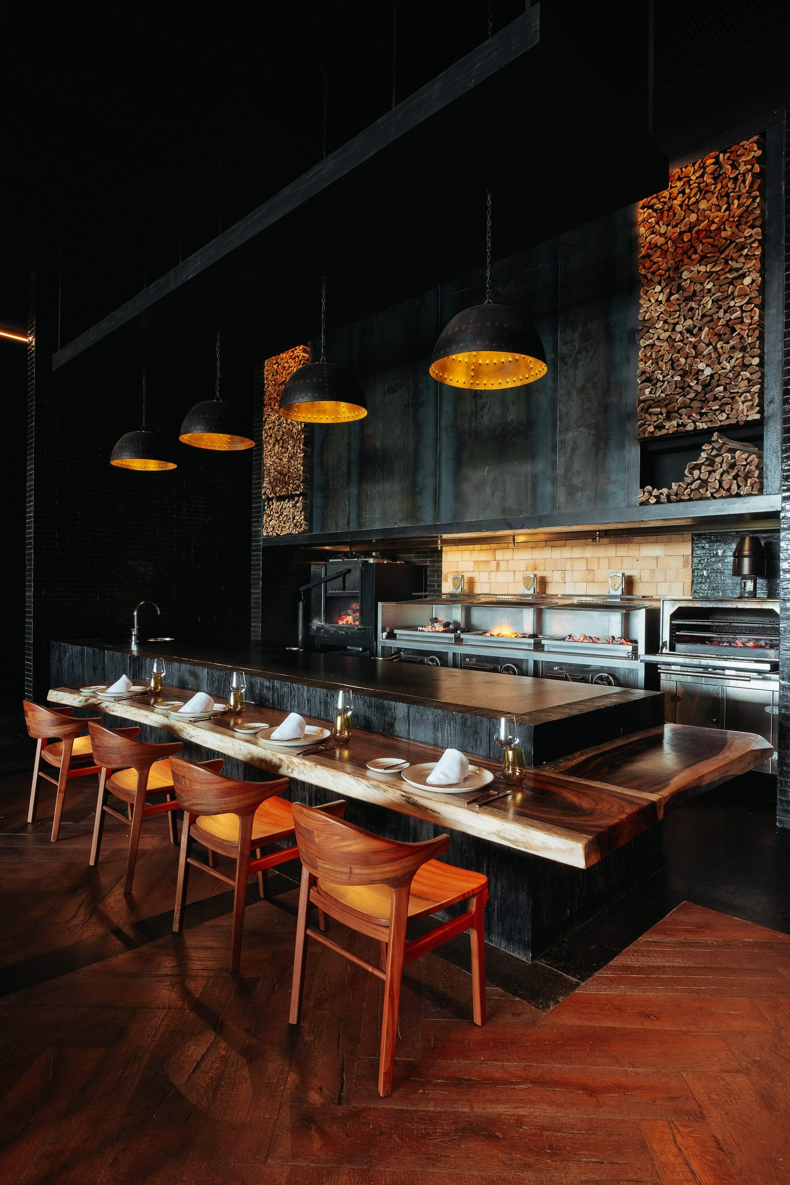 A modern restaurant with a long counter, wooden chairs, and pendant lighting.