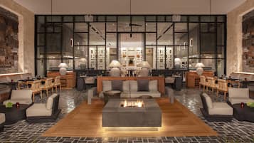 A modern lounge area with a central fire feature, seating arrangements, and a view of the kitchen through large windows.
