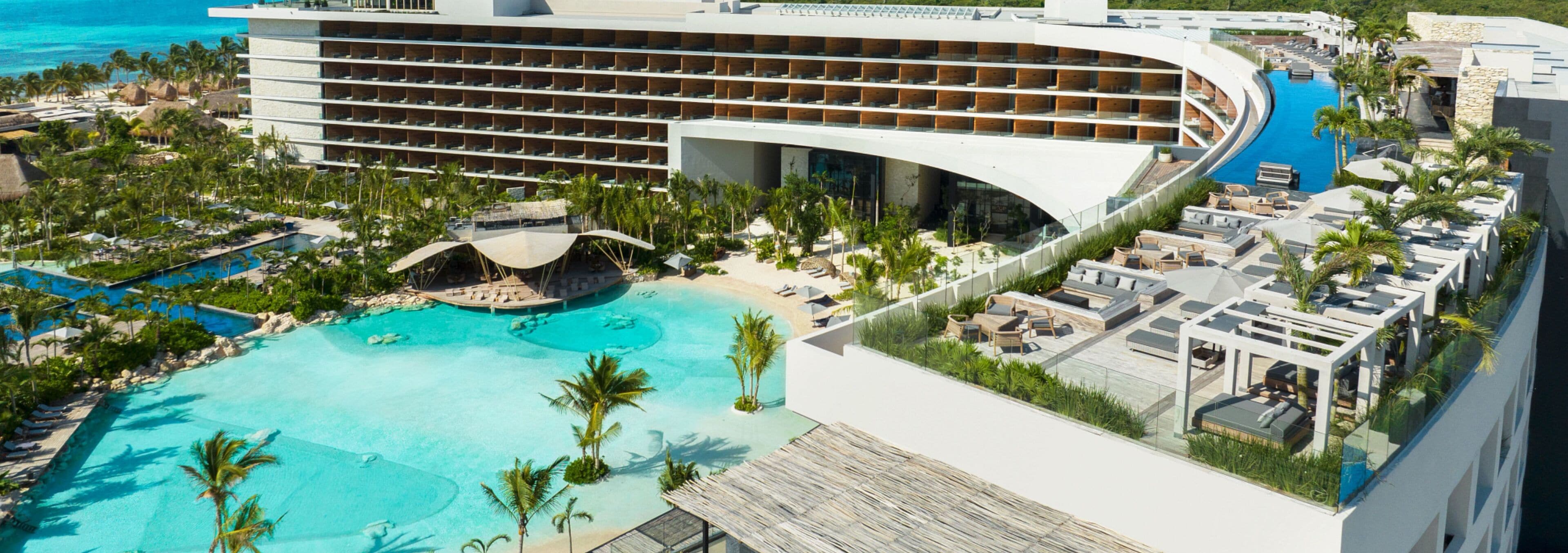 A modern resort with a large pool, multiple balconies, and a beach area.