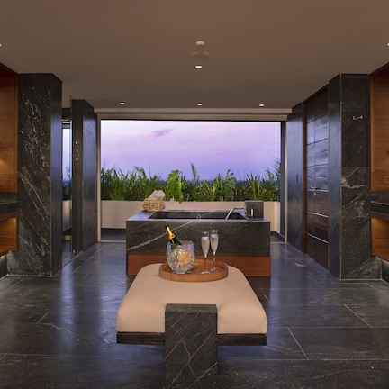 A modern bathroom with a large bathtub, a vanity with a mirror, and a seating area with a bottle of champagne and glasses.