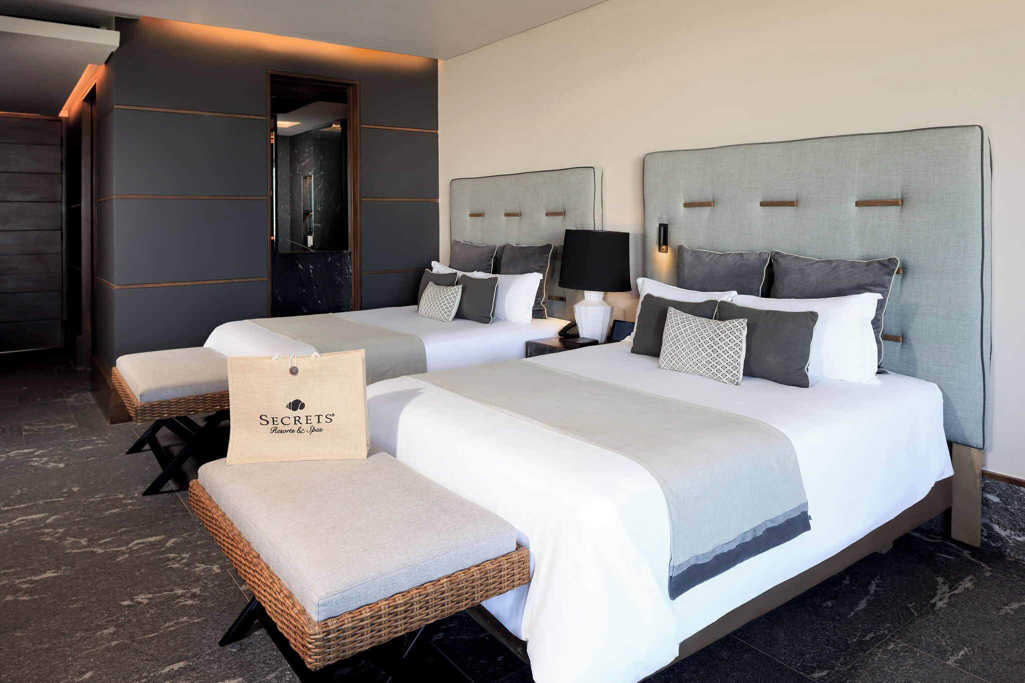 Una habitación de hotel con dos camas, un espejo grande y una silla de mimbre.