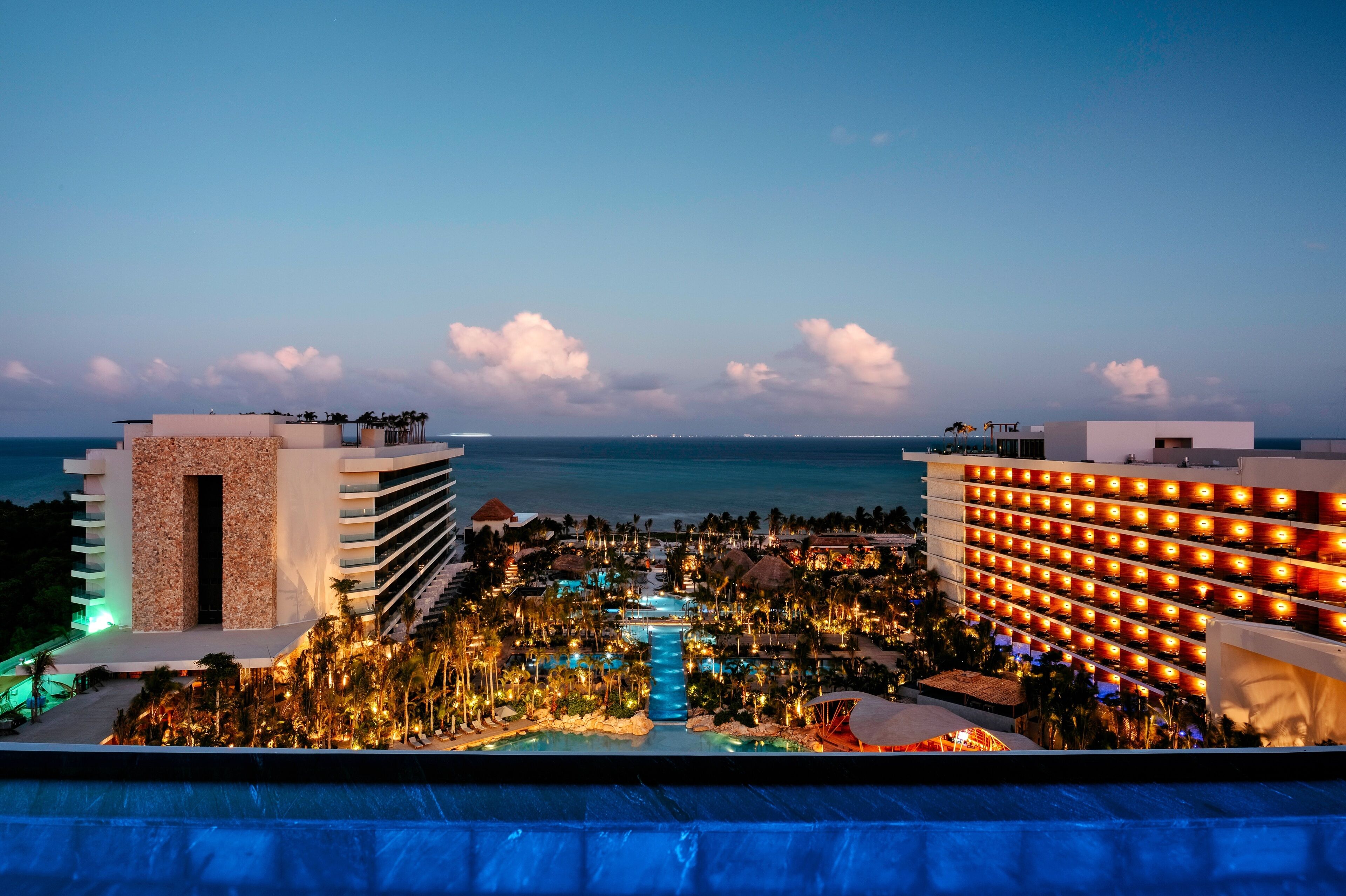 Un resort con zona de piscina, vista al océano y un edificio con una hilera de luces.