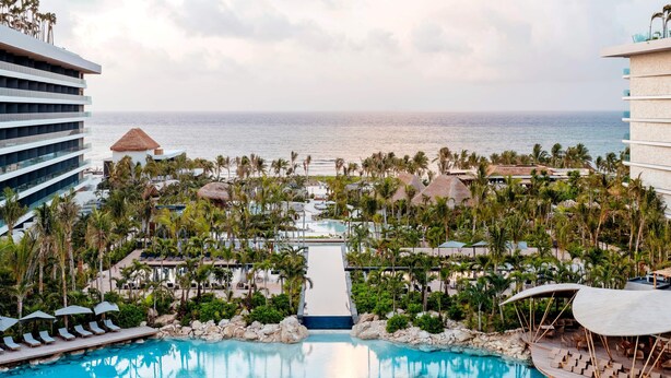 Un resort con piscina central, palmeras y vistas al océano.