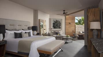 Una habitación de hotel moderna con una cama grande, una zona de estar con una mesa y sillas, un ventanal con vista a palmeras y un ventilador de techo.