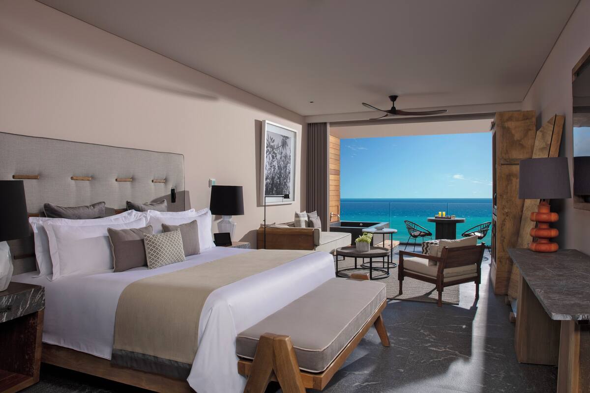 Una habitación de hotel moderna con una cama grande, un escritorio, una silla y vistas al océano.