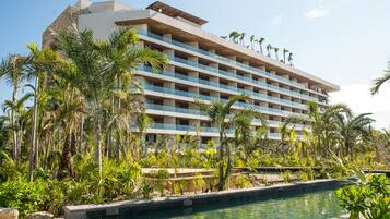 Un hotel de varios pisos con piscina rodeada de palmeras y vegetación.