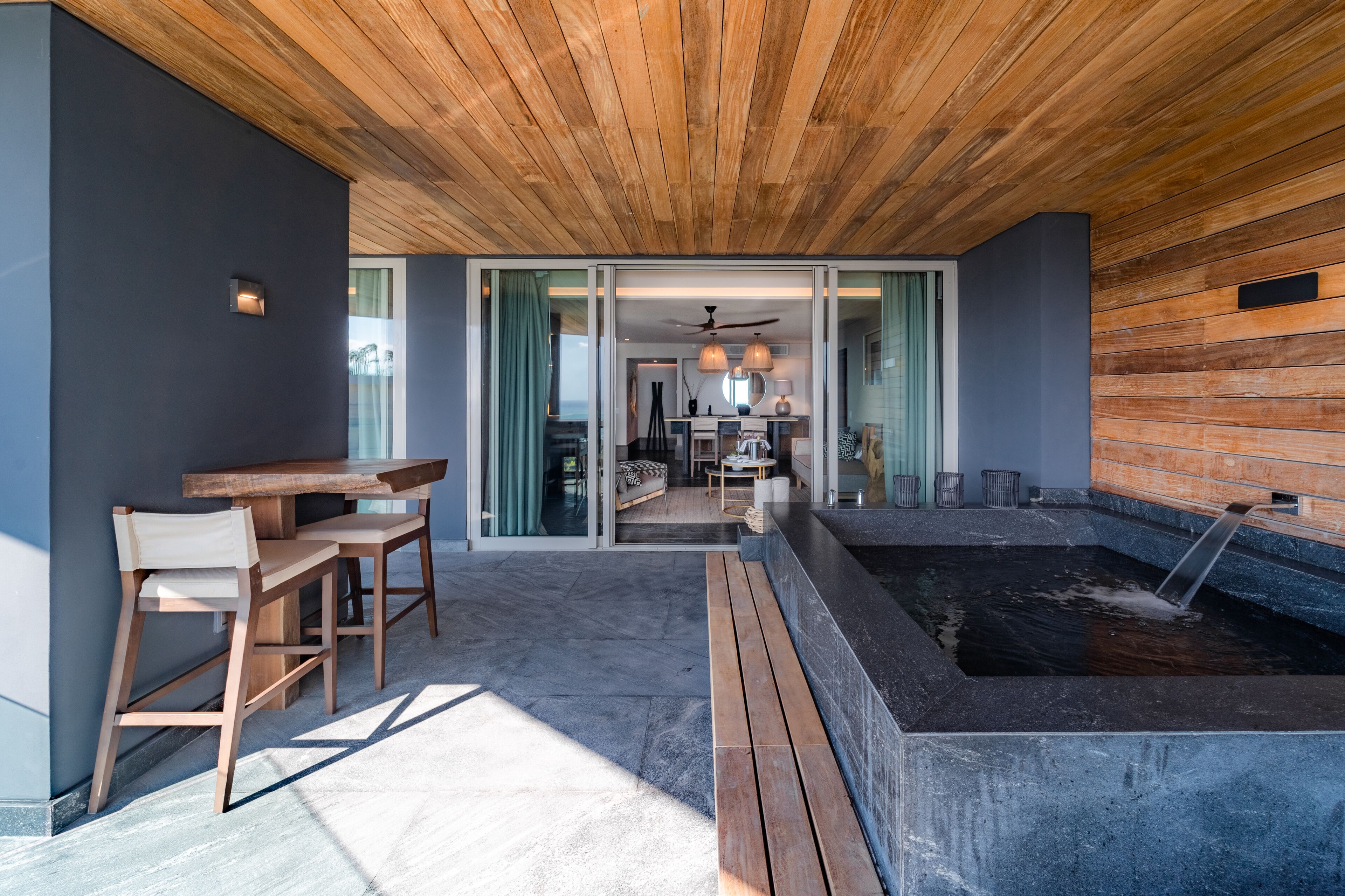 Un patio moderno al aire libre con mobiliario de madera, un jacuzzi y vista hacia la casa.