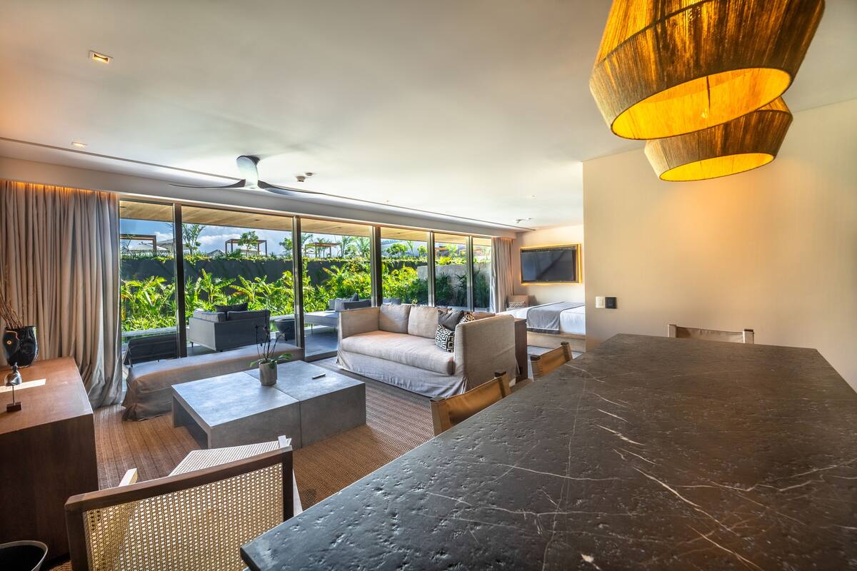 Un salon moderne doté d’une grande table en marbre foncé, de sièges confortables et de larges fenêtres offrant une vue sur la verdure.
