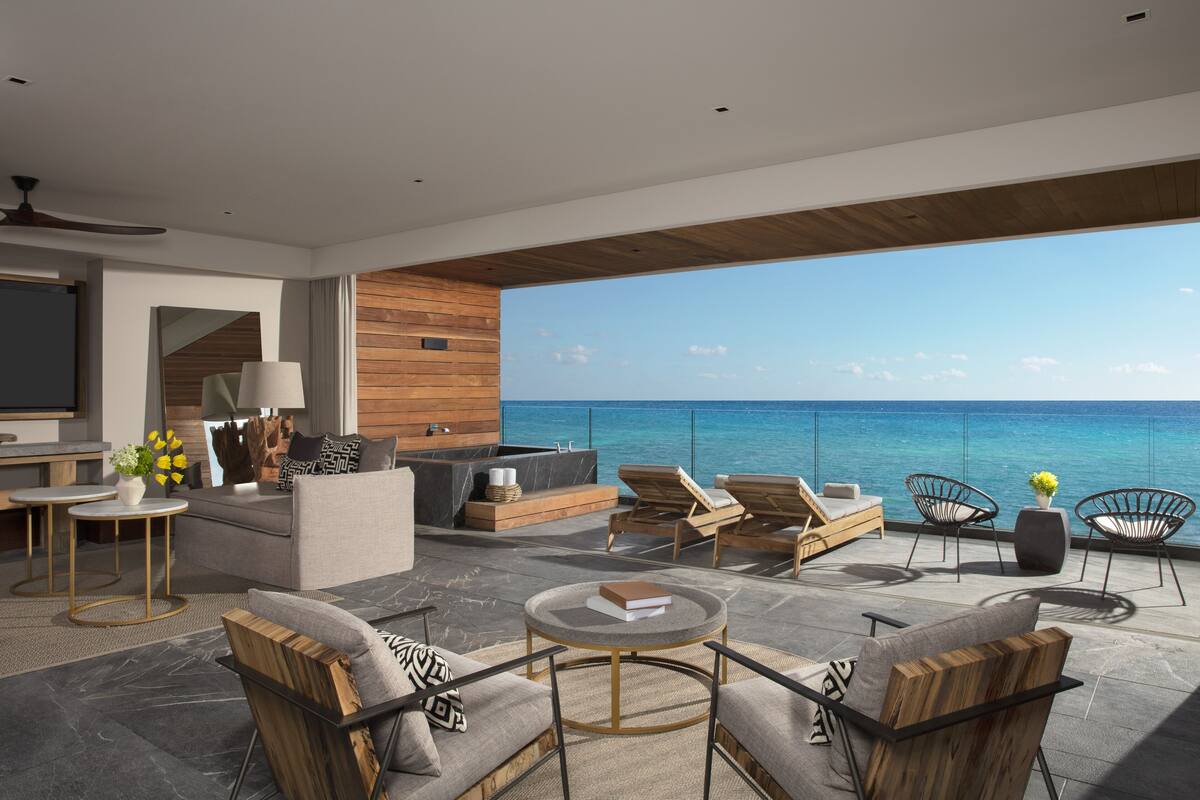 Un espace de vie extérieur moderne avec vue sur l’océan, aménagé avec des canapés, des fauteuils et une petite table.