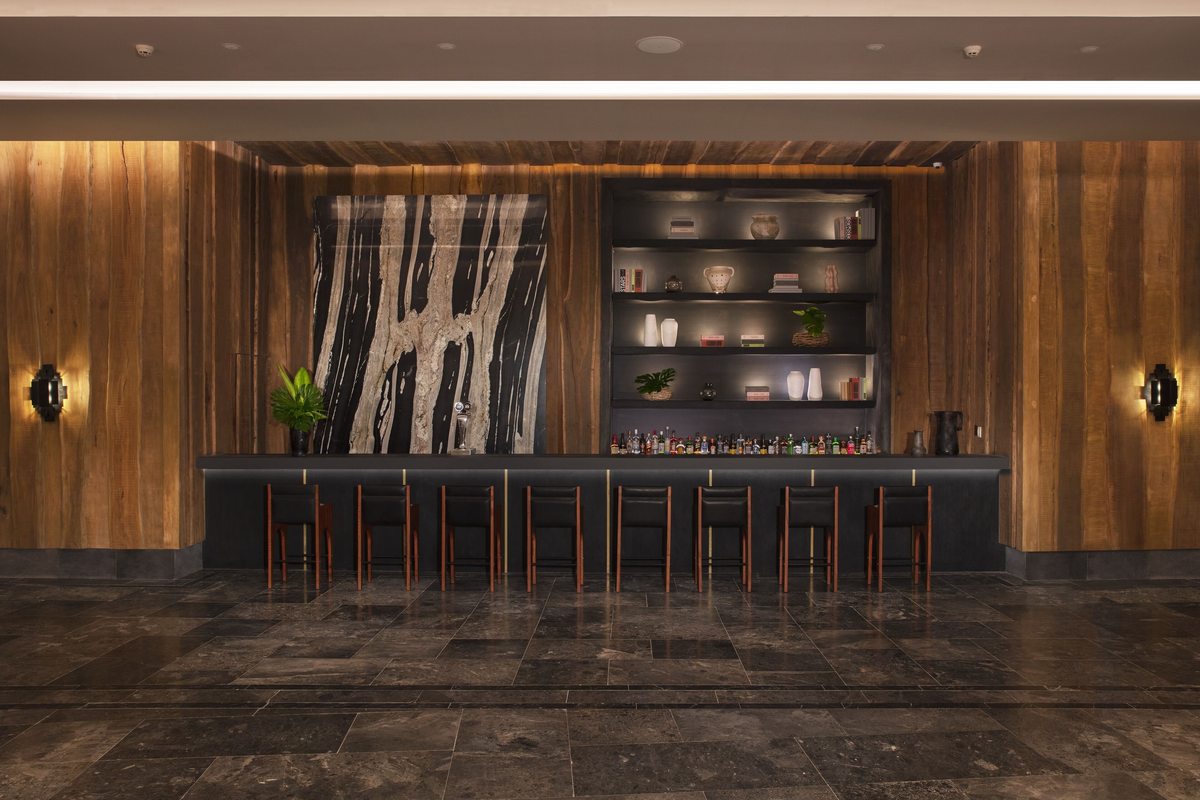 A bar area with a wooden backdrop, a large abstract painting, and shelves with various items.