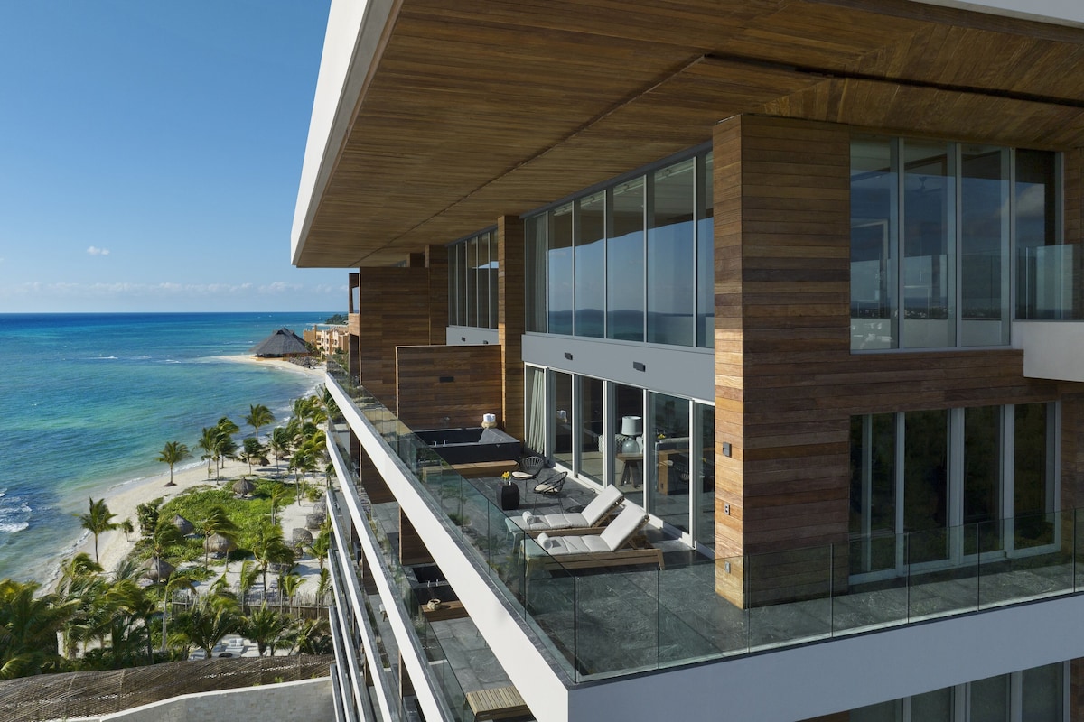 Un hotel moderno con balcón de vidrio que da a una playa y al océano.