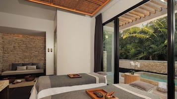 A modern bedroom with two beds, a stone wall, a wooden ceiling, and a view of a pool and greenery.