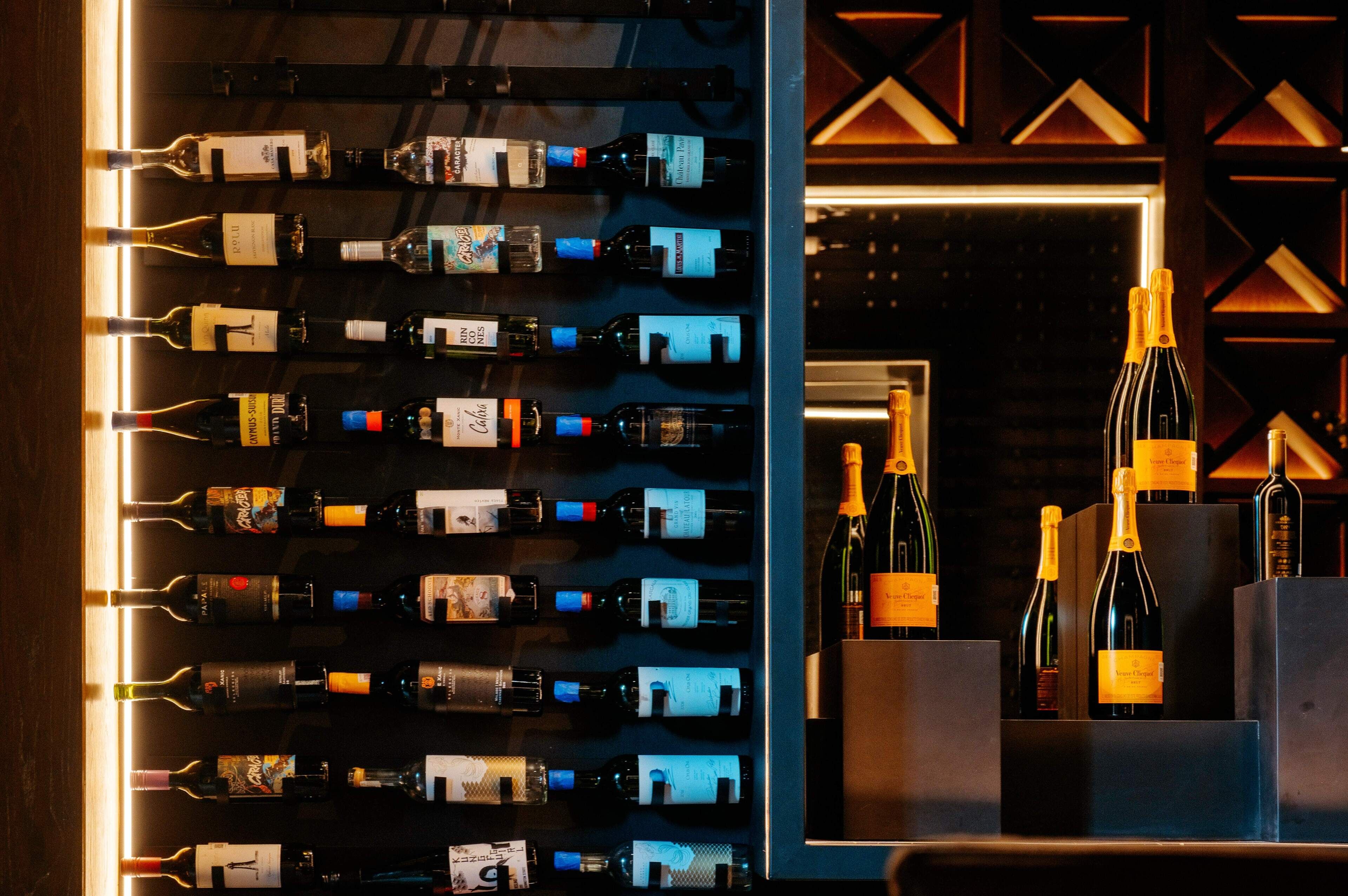 Una alacena para vinos con varias botellas, una zona de bar con botellas y un diseño geométrico en la pared.