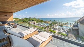 Een balkon met houten meubilair en uitzicht op een resort, inclusief een zwembad en de oceaan.