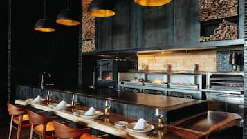 A modern restaurant with a long counter, wooden chairs, and pendant lighting.