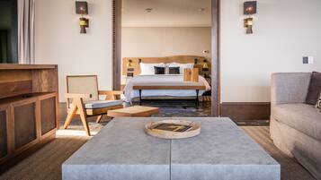 A hotel room with a bed, a wooden nightstand, a grey sofa, a coffee table, and a TV.