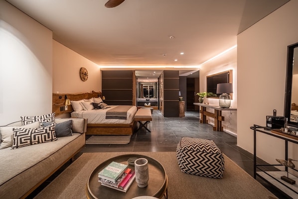 Una habitación de hotel moderna con sofá, cama, una mesita de centro con libros y un adorno en la pared.