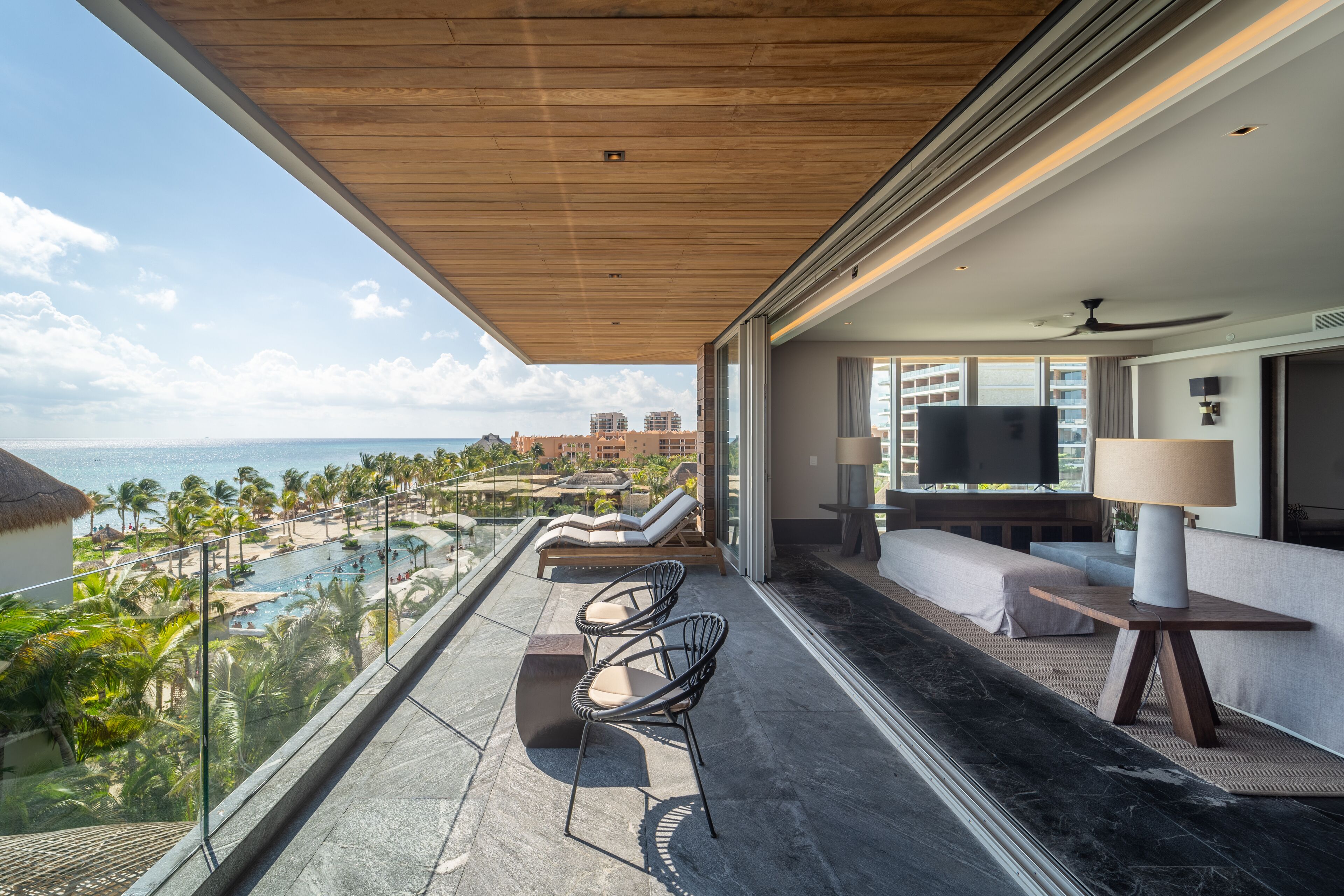 A balcony with a view of a pool and beach, furnished with chairs and a sofa.