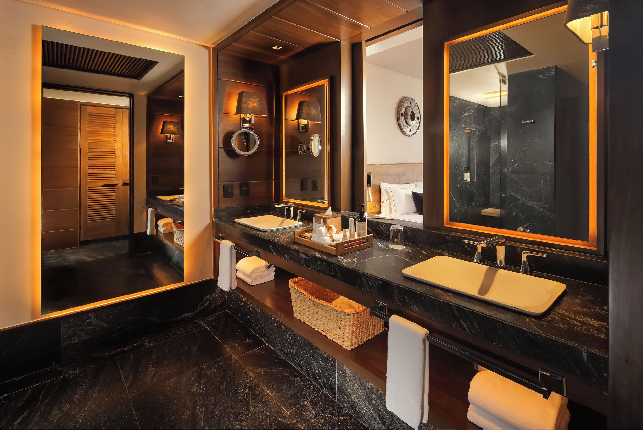 A modern bathroom with dark marble countertops, two sinks, and large mirrors. There are towels and toiletries on the counter.