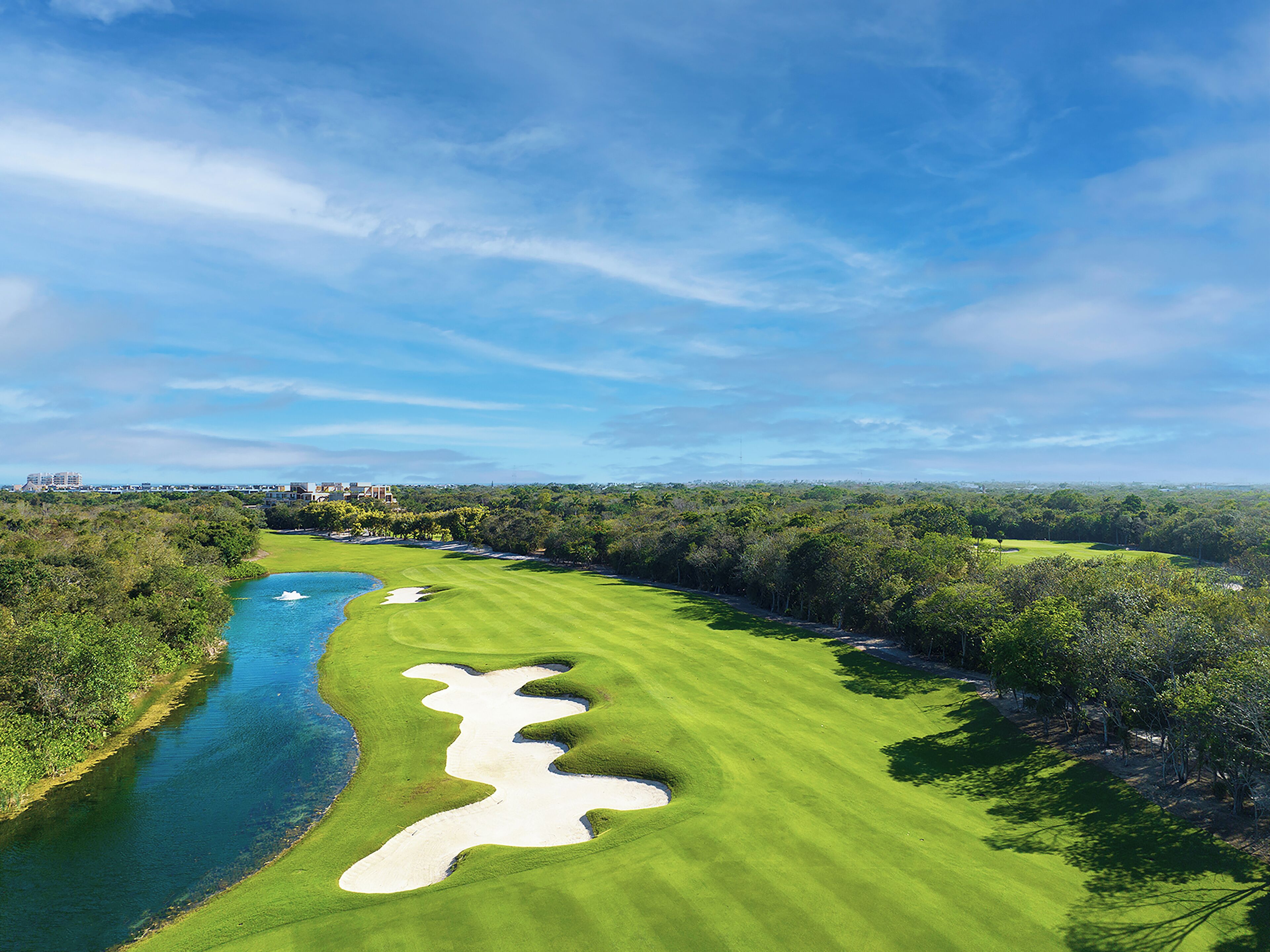 Un parcours de golf avec une rivière, des bunkers de sable et une végétation dense.