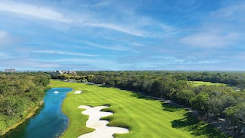 Un parcours de golf avec une rivière, des bunkers de sable et une végétation dense.