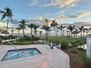 A pool area with lounge chairs, a small pool, palm trees, and a beach view.