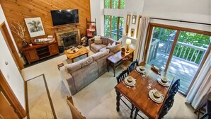 A spacious living area with a fireplace, a television, and a dining table set for four. - Mountain condo by Okemo w/ hot tub (Ludlow)