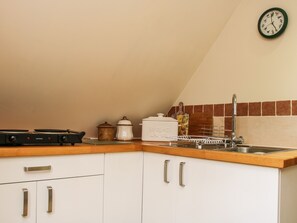 Eine Küche mit weißen Schränken, einer Holz Arbeitsplatte, einem Gasherd, einem Wasserkocher, einer Brotdose und einer Wanduhr.