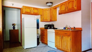 A compact kitchen with wooden cabinets, a refrigerator, a microwave, and a stove. - Julieann's in Alaska - Home in the Heart of Sitka (Sitka)
