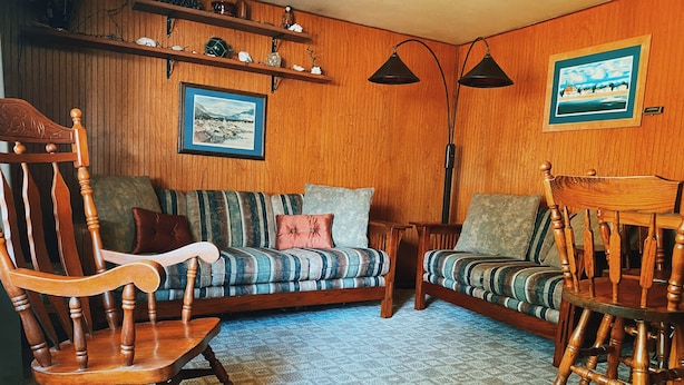 A cozy living room with a wooden floor, a striped sofa, a rocking chair, a small table, and two wall-mounted lamps. - Julieann's in Alaska - Home in the Heart of Sitka (Sitka)