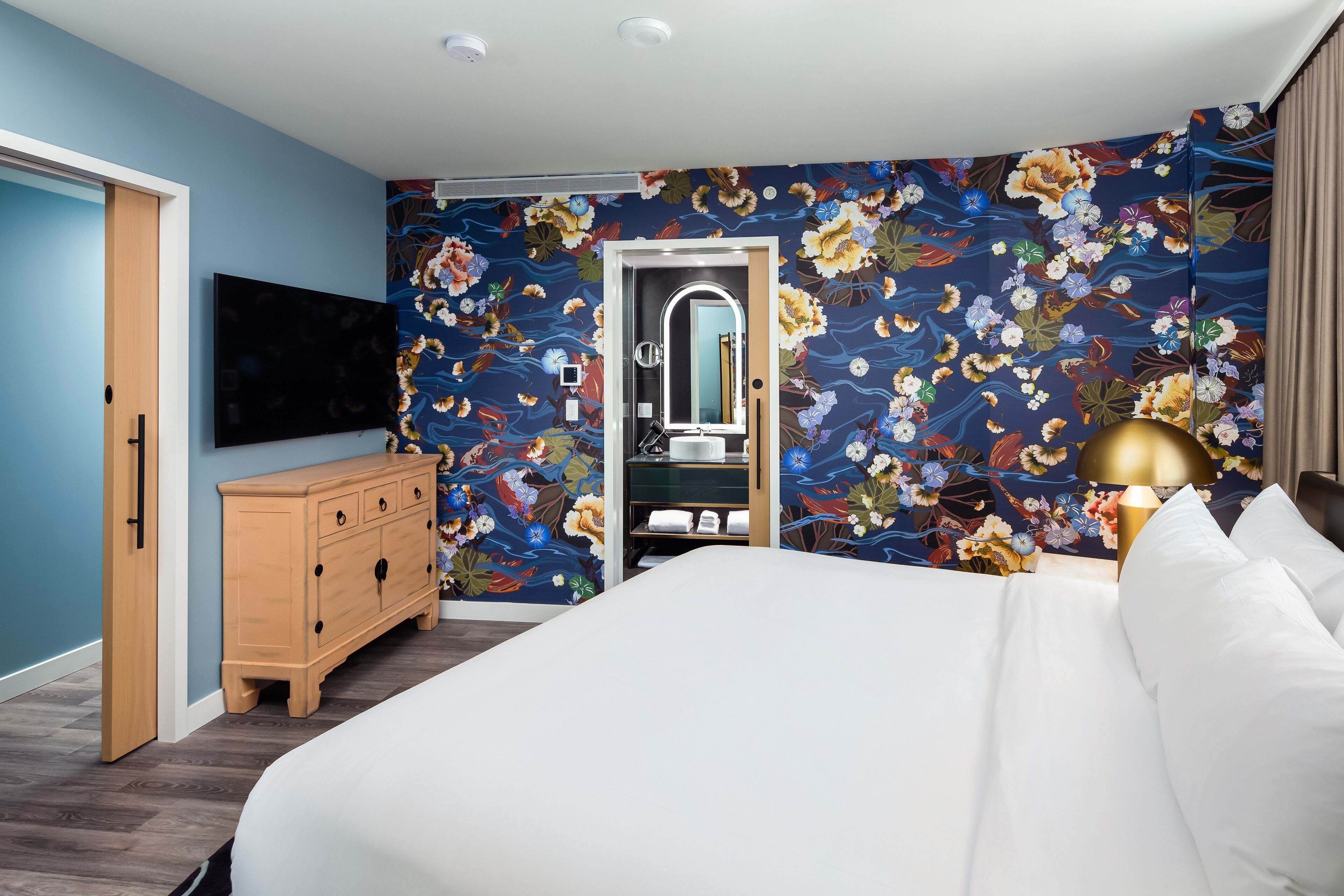 A hotel room with a bed, a dresser, a TV, a mirror, and a bathroom with a shower.
