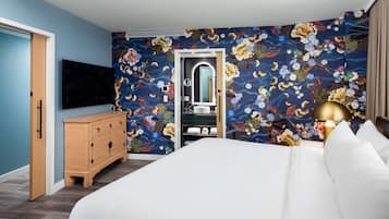 A hotel room with a bed, a dresser, a TV, a mirror, and a bathroom with a shower.
