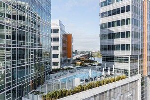 Un edificio moderno con piscina en la azotea, barandillas de cristal y vista a un puente.